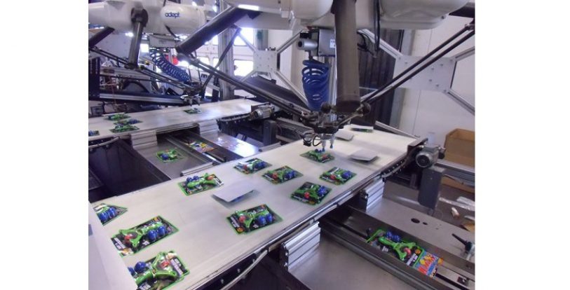 Zwei Deltaroboter greifen die Teile und kleben sie mit einem Druckluftimpuls auf die vorbeilaufenden Zeitschriften.