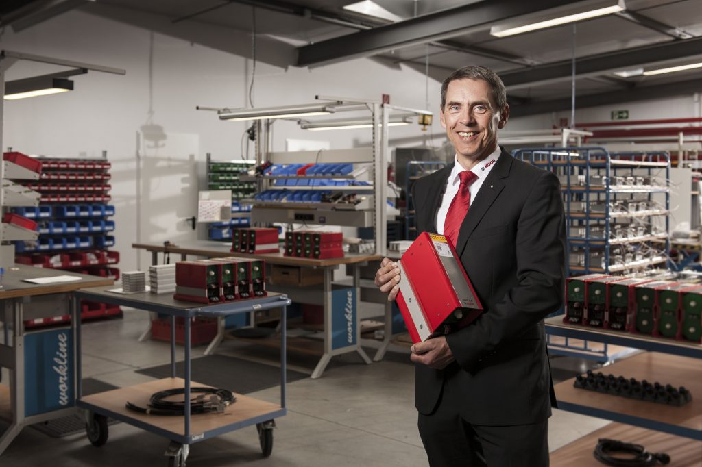 Mit einem Dynamischen Energiespeicher DES in Händen inmitten des Fabrikle.