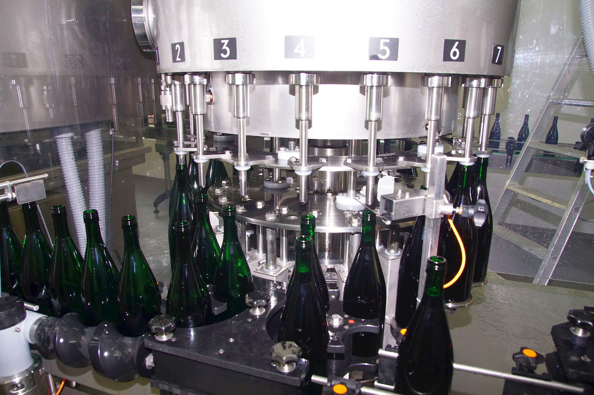 Im Falldruckfüller werden die Flaschen an die konischen Füllventile angepresst, zentriert und fixiert. Der Wein strömt vom Füllerkessel durch ein feinporiges Füllrohr in die Flasche. (Bild: broesele)