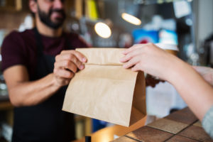 Mann reicht Take-away Papiertüte über Tresen