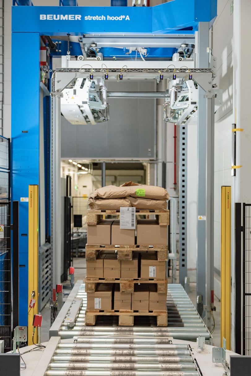 Über Rollenbahnen kommen die palettierten Waren sicher in die Verpackungsanlage. (Bild: Beumer)