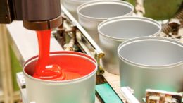Eine Weißblechdose wird maschinell mit roter Farbe gefüllt