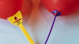 Zwei rote Luftballons, die mit Papierhaltern versehen sind. Der linke ist gelb und trägt das Logo von McDonald's
