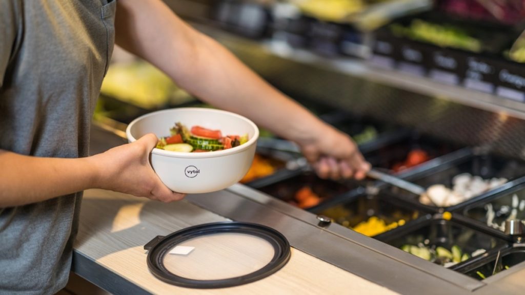 Eine Kunststoffschale wird an der Salatbar befuellt.