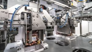 Ein Roboter übernimmt eine Schokoladentafel von Ritter Sport und setzt sie auf den Kopf gestellt in den Deckel des Kartons ein.