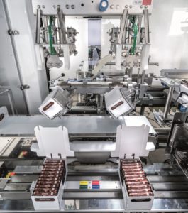 Verkaufsfertige Ritter-Sport-Schachteln werden um 180 Grad gedreht und auf ein Auslaufband gesetzt.