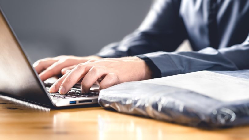 Laptop mit Händen und Plastikverpackung Retourenflut