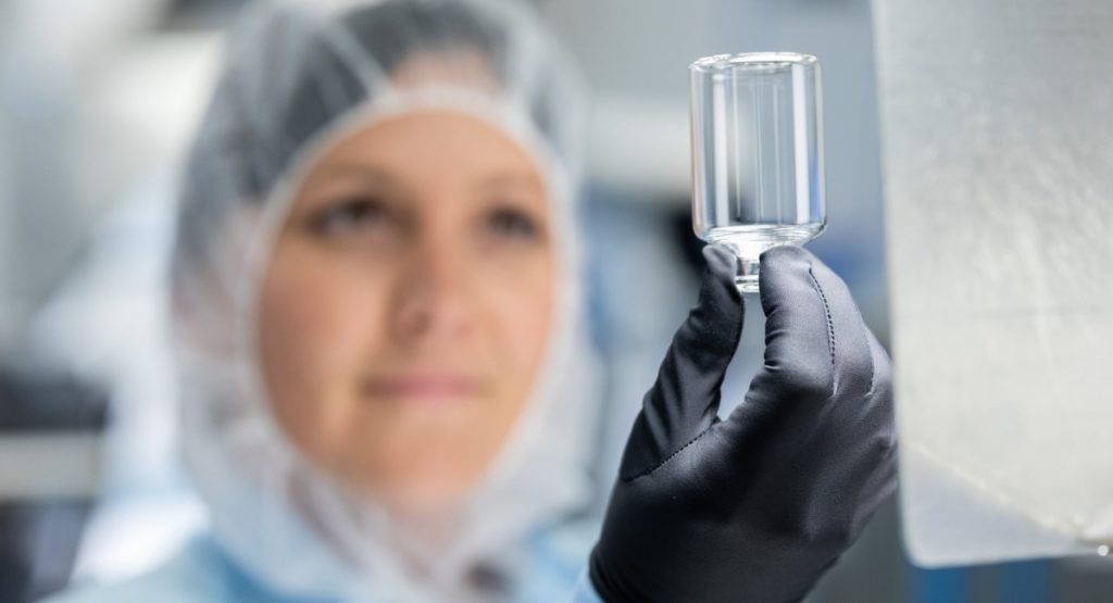 Frau mit Schutzhaube hält Pharmaglas Vial