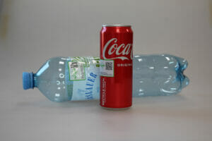 Hinter einer roten Cola-Dose liegt eine Plastikflasche. Beide Getränkeverpackungen sind mit einem Qr-Code beklebt.