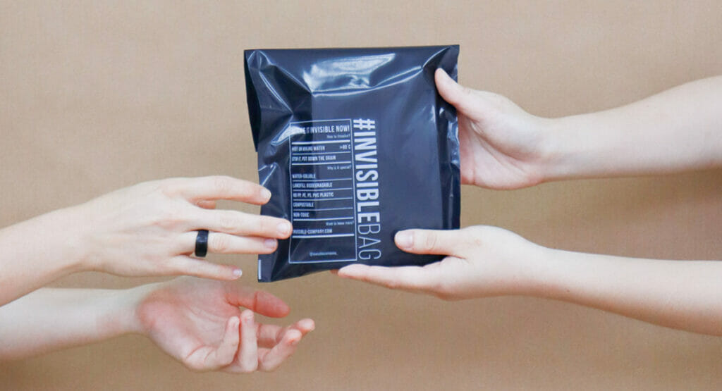 Ein Biokunststoff-Versandbeutel der Invisible Company, gehalten von vier Händen
