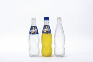 Drei Prototypen von Orangina in der PET-Flasche aus 100 Prozent pflanzlichen Materialien von Suntory stehen nehmen einander. Die linke Flasche ist leer und trägt ein Etikett, die mittlere Flasche trägt ein Etikett und ist mit Orangina gefüllt, während die rechte Flasche leer und ohne Etikett ist.