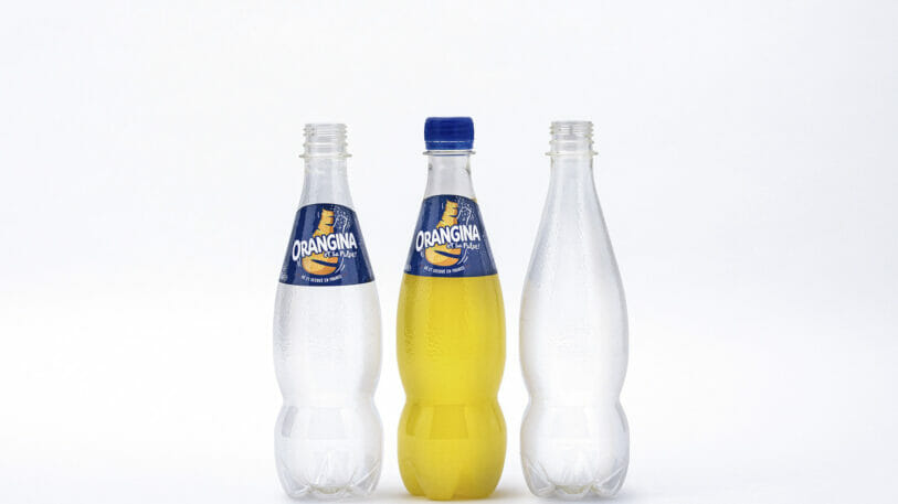 Drei Prototypen von Orangina in der PET-Flasche aus 100 Prozent pflanzlichen Materialien von Suntory stehen nehmen einander. Die linke Flasche ist leer und trägt ein Etikett, die mittlere Flasche trägt ein Etikett und ist mit Orangina gefüllt, während die rechte Flasche leer und ohne Etikett ist.