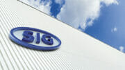 Das Firmenlogo von SIG Combibloc ist auf einem Gebäude zu sehen mit blauem Himmel und Wolken im Hintergrund.