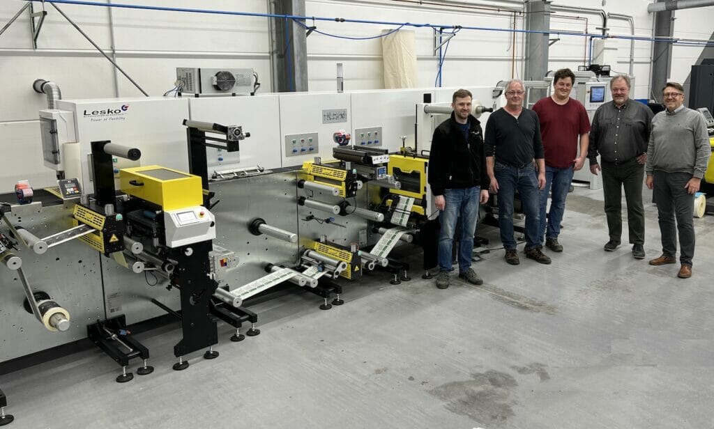 Bild von fünf Männern in einer Produktionshalle vor einer Maschine.