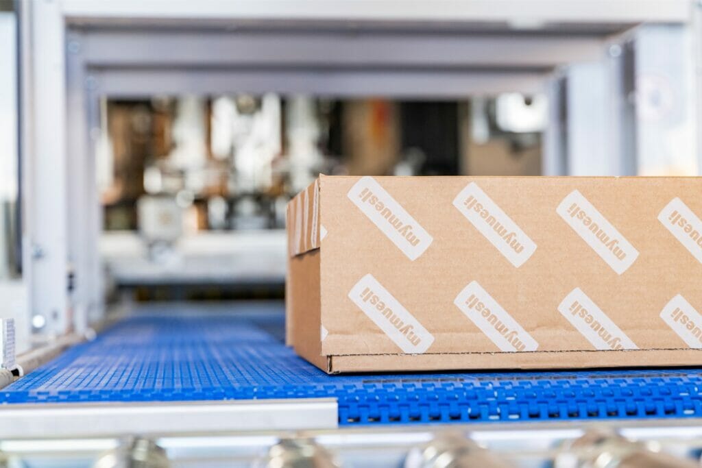Versandkarton von mymuesli, der über ein blaues Rollband fährt.