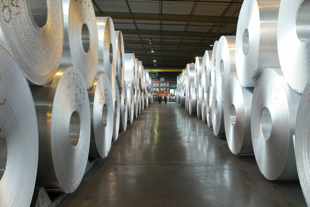 MANY large rolls of aluminium are stacked in a warehouse.