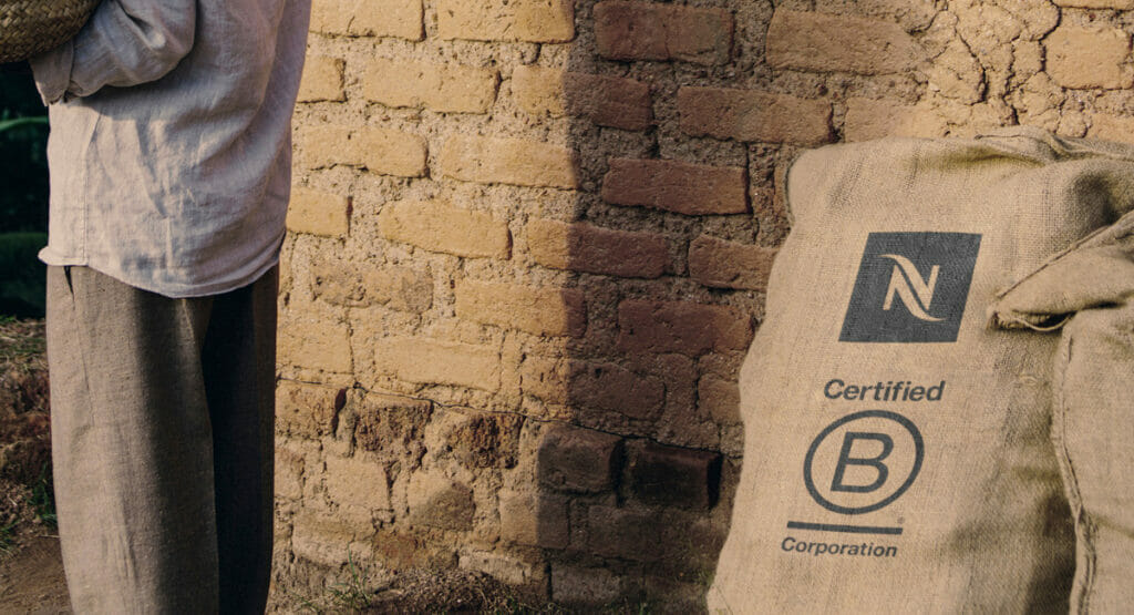 Bild von einer Ziegelwand von einem Haus, an der ein Sack mit dem Logo von Nespresso und der B-Corp-Zertifizierung lehnt. An der Wand geht eine Person vorbei.