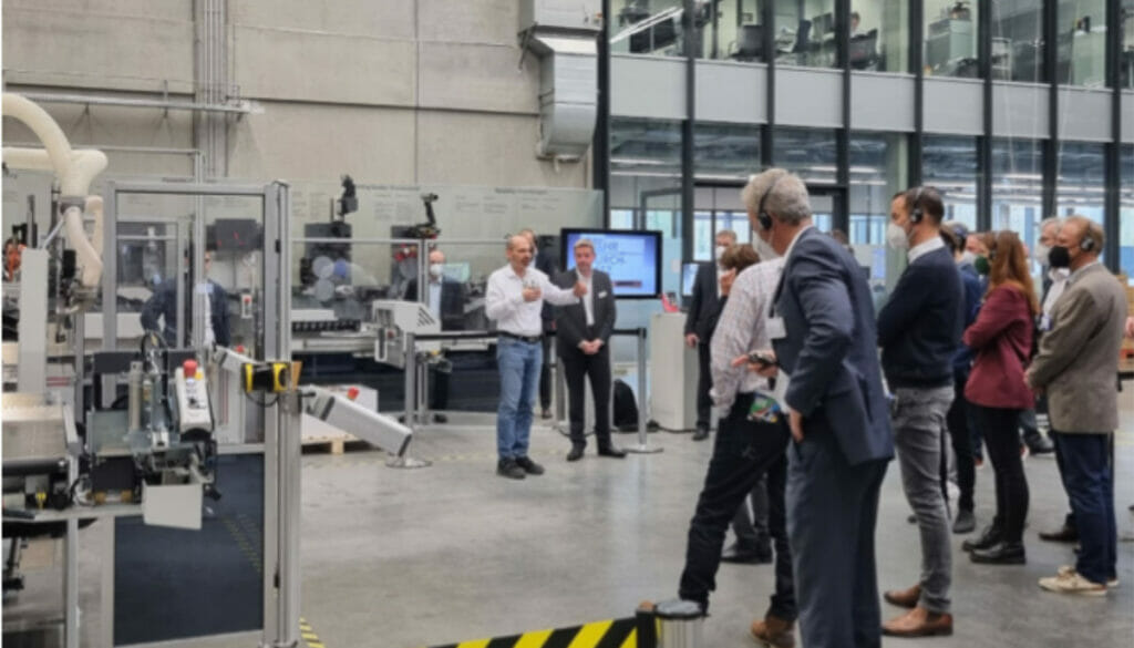 Bild von einer Halle mit vielen Menschen, die eine Produktvorstellung ansehen.