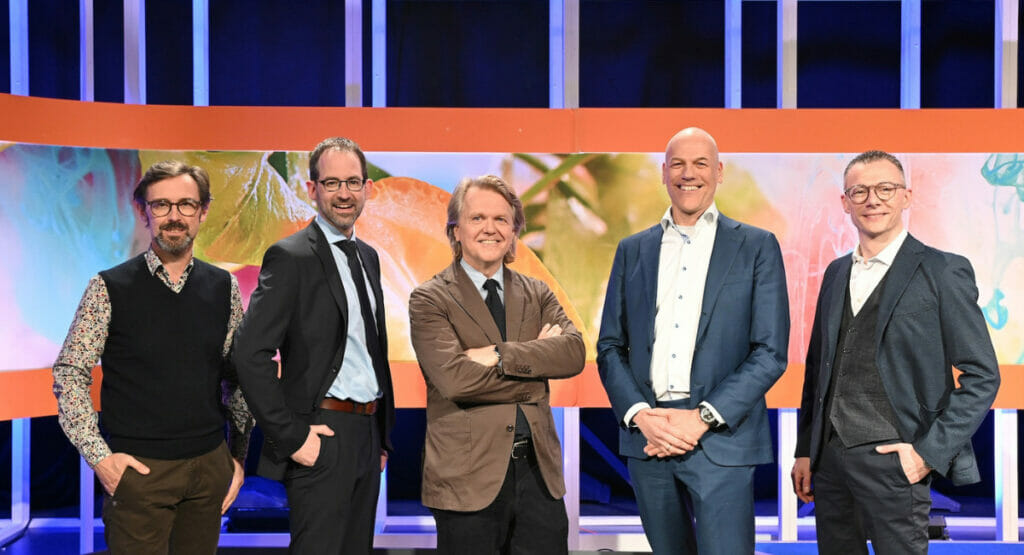 Bild von fünf Männern, die in einer Reihe stehen und in die Kamera lachen.