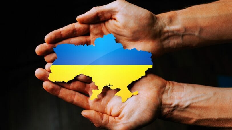Two hands are holding a piece in the shape of Ukraine