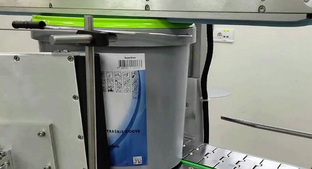 Bild von einem Farbeimer, der in einer Maschine etikettiert wird.