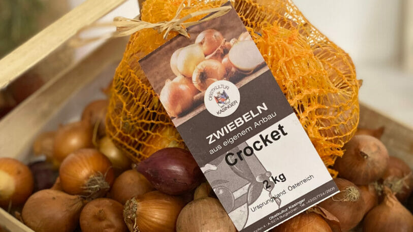 Bild von einem Sack mit Zwiebeln und einem Etikett, die auf losen Zwiebeln liegen.
