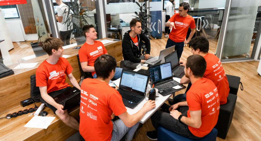 Bild von einer Gruppe von Menschen, die einer Person zuhören und an Laptops arbeiten