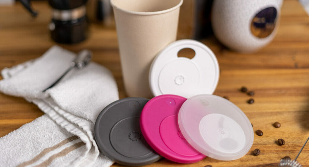 Bild von einem Tisch, auf dem vier wiederverschließbare Mehrwegdeckel und ein Becher aus Papier stehen.