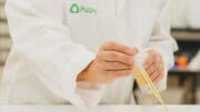 Bild von einer Person im Laborkittel, die eine Pipette mit Flüssigkeit in der Hand hält.