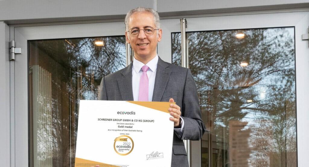 Bild von einem lachenden Mann, der vor einem Gebäude steht und eine Auszeichnung in den Händen hält.