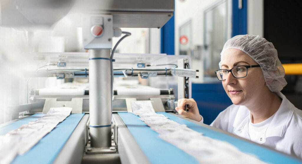Bild von einer Frau in Arbeitskleidung, die vor einer Sachet-Anlage steht.