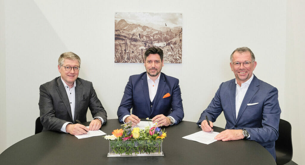 Bild von drei Männern, die an einem Tisch sitzen und Dokumente unterschreiben.