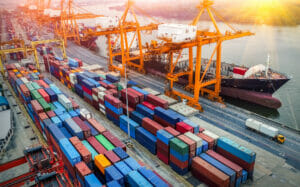 Bild von einem Hafen, mit Containern und Kränen, die Ware verladen.