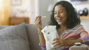 Bild von einem Mädchen auf einer Couch, das Chips aus einer Tüte isst.