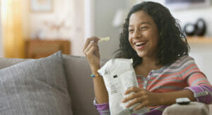 Bild von einem Mädchen auf einer Couch, das Chips aus einer Tüte isst.
