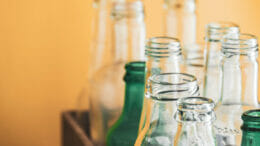Bild von unterschiedlichen Glasflaschen vor einem orangefarbenen Hintergrund.