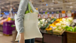 Bild von einer Person, die einen gefüllten Einkaufsbeutel über der Schulter trägt und durch den Supermarkt geht.
