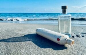 Bild von einer Aluminium- und einer Glasflasche, die am Meer liegen