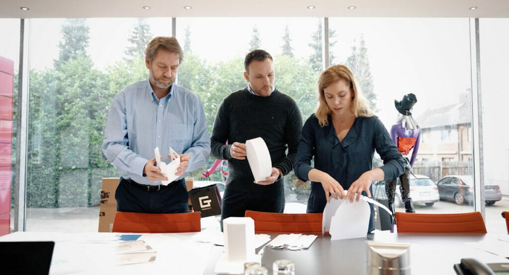 Image of two men and a woman standing at a table and looking at packaging designs.