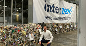 Bild von einem Mann, der vor einem Banner mit einem Firmenlogo und sortenreinen Abfallballen kniet