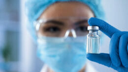 Image of a woman in protective clothing holding a glass vial