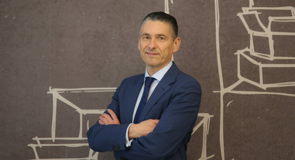 Bild von einem Mann vor einer Wand, der in die Kamera lacht