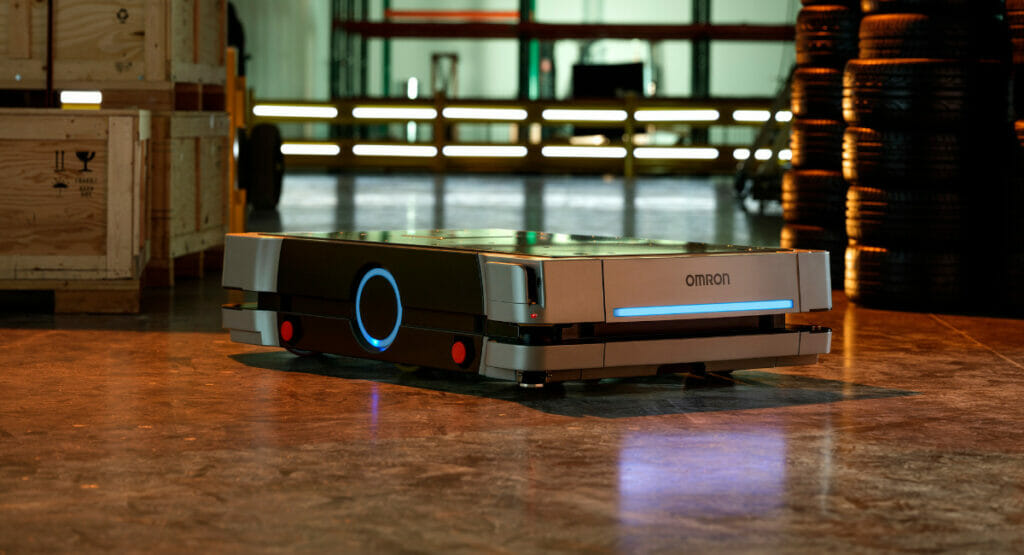 Ein Omron-Transportroboter steht zwischen einem Palettenstapel und einem Haufen Gummireifen.